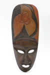 Máscara tribal de parede em madeira, composta verticalmente com figura antropomórfica central sobreposta por elementos simbólicos em relevo na tonalidade escura e mel. Verso escavado. 91x22 cm.