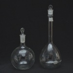 Conjunto com dois vidros de laboratório Pyrex (USA), em vidro borossilicato transparente. Composto por frasco volumétrico graduado de 1000 ml (calibrado a 20 C) e frasco esférico, ambos com tampa esmerilhada. Peças destinadas ao preparo, medição preciso de soluções químicas. Também valorizados como objetos decorativos. 35 e 23 cm altura