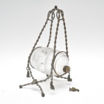 Barril decorativo em vidro espesso, ricamente acidado (fosqueado) com delicada decoração contínua de parreiras, folhas e cachos de uvas, corpo cilíndrico com  anéis lapidados nas extremidades.A peça encontra-se suspensa e apoiada em elaborado suporte de ferro fundido, trabalhado em barras retorcidas,  motivos florais, além de alça superior decorada com contas e folhas estilizadas, evidenciando clara inspiração naturalista, típica do final do século XIX / início do século XX. Torneira solta, no estado. 32x17x18 cm