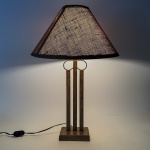 Abajur em metal, com haste vazada de desenho geométrico e base quadrangular. Acompanha cúpula em tecido. Estrutura com pátina em tom terroso. 63x40 cm (com a cupula).