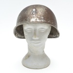 Capacete militar em aço prensado,  com aba contínua, acabamento em pintura verde-oliva fosca, típico de uso operacional. Apresenta rebite superior central e borda enrolada, características técnicas para serviço de campanha. O interior conserva parte do sistema original de suspensão, com presilhas metálicas laterais e tira de couro central. Caracteristicas construtivas, desenho e acabamento,  de um capacete utilizado entre as décadas de 1930 e 1950, período que abrange a Segunda Guerra Mundial e o pós-guerra imediato, quando modelos desse tipo foram amplamente empregados por forças militares e, em alguns casos, por corpos auxiliares e de defesa civil.