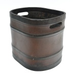 Elegante lixeira ovalada confeccionada em espesso couro natural, com costura manual aparente em ponto cruz, executada com linha grossa, conferindo refinamento e solidez à peça. Corpo estruturado por faixas horizontais moldadas e empunhadura vazada lateral. Base com marca em baixo-relevo OTA  Rio  Brasil. Patina original, com discretas marcas do tempo. 29x27x25 cm