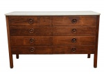 Sergio Rodrigues - comoda de frente composta por oito gavetas dispostas em dois corpos verticais, cada uma com puxadores circulares torneados, elemento recorrente no vocabulário moderno brasileiro do período. Tampo em mármore claro, solto, assentado sobre a estrutura. Parte posterior do tampo apresenta inscrição manuscrita atribuída aLoja Cantú- década de 1960 (Moderno Brasileiro). Apresenta partes do laminado se desprendendo e no tampo algumas  ausencias. 130x50x81 cm