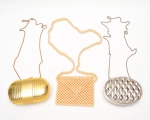 Lote com três bolsas tipo toalete para festa, de estilos distintos, sendo uma bolsa em contas peroladas, com alça longa, uma bolsa rígida metálica dourada, de formato oval alongado, com superfície canelada e acabamento acetinado e uma  bolsa rígida metálica prateada, oval, com relevo geométrico facetado em padrão losangular, 62x15 cm com alça/ 65x12x6 cm com alça/ 67x17x7 cm com alça