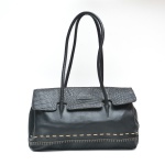 Bolsa de couro preta, confeccionada em couro liso combinado a couro com textura croco na aba frontal. Apresenta alças duplas de ombro, costuras aparentes em tom claro na base, fecho por botão magnético. O interior é forrado em tecido bege personalizado com monograma da marca Swains. Bom estado de conservação. 56x43 cm com a alça