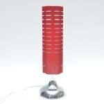 Luminária retrô  de mesa em metal, composta por corpo cilíndrico vertical com pintura esmaltada em tom vermelho intenso. A cúpula tubular apresenta frisos verticais ritmados e cortes horizontais vazados que permitem a difusão lateral da luz. Estrutura apoiada sobre base circular chrome brillant. Muito decorativa, de forte presença visual, e apelo pop. Fiação revisada e funcionando. 41x14 cm