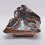 Anos 70 - Centro de mesa em cerâmica modelada à mão, de forma livre e orgânica, com recortes e dobras esculturais que criam um efeito de movimento, com esmaltação típica do estilo pingo de leite, em tons de marrom terroso com manchas azuladas esbranquiçadas. 18x17x14 cm