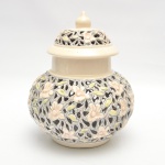 Potiche em cerâmica vitrificada, de corpo globular e tampa abaulada com pináculo. Apresenta delicado trabalho vazado em relevo, com flores e folhas modeladas e esmaltadas em tons de marfim, verde e cinza-azulado. 28x22 cm diam.