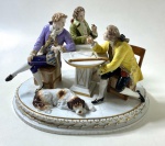 SAXE-ALEMANHA - SÉC XIX -  GRUPO EM PORCELANA DE SAXE RICAMENTE TRABALHADO COM TRÊS FIDALGOS CONVERSANDO AO REDOR DE UMA MESA E UM CACHORRO DORMINDO AOS PÉS DELES. MEDIDAS: 18 X 25 CM