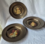 Três grandes pratos de aparato em metal ao centro em reserva reproduções de pinturas de grandes mestres medindo 43 cm de diâmetro por 5 cm de altura marcados e selados no verso.