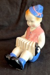 Escultura em porcelana  policromada representando menino com folê, medindo 14 cm de altura por 11 cm por 9 cm na base, perfeito estado de conservação.
