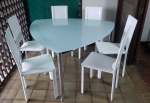 Mesa no formato triangular, pés em metal cromado, tampo em vidro e 6 cadeiras em couro sintético branco. Etiqueta Tok Stock. Mesa Alt. 75 x diam. 140cm e cadeira 92 x 40 x 40cm.