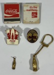 Lote com 6 itens colecionáveis Coca-Cola sendo 2 broches, 1 das Olimpíadas de 2016 do Rio, outro das Olimpíadas de 1996 de Atlanta. 1 chaveiro em formato de uma garrafa de Coca-Cola na cor dourada, 1 pingente em formato de garrafa de Coca-Cola na cor dourada e 2 caixas de fósforos da marca produzidos pela American Match Co. NY
