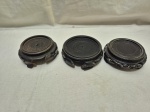 Conjunto com três bases orientais em madeira entalhada, de formatos variados e acabamento escuro, destinadas à exposição de vasos ou esculturas, apresentando sinais de uso e pequenas falhas. Medindo o maior 7cm interno x 10,5cm externo.