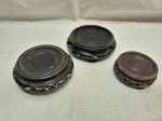 Conjunto com três bases orientais em madeira entalhada, de formatos variados e acabamento escuro, destinadas à exposição de vasos ou esculturas, apresentando sinais de uso e pequenas falhas Medindo o maior 7,5cm interno x 11cm externo.