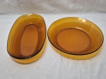 Jogo de 2 travessas, sendo uma oval e uma redonda em vidro Duralex. Medindo 28,5cm x 5cm de altura; 34cm x 19cm x 5cm de altura. Com pequenos bicados.