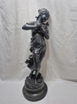 Escultura feminina em prata 90, representando uma jovem segurando um pássaro junto ao peito, com outro pousado no ombro. A peça tem estilo Art Nouveau, com linhas suaves e expressão delicada. A base é em mármore, sólida e bem trabalhada. A escultura está em bom estado, com desgaste mínimo natural do tempo. Medindo 56cm de altura.