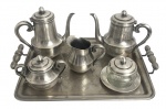 Conjunto de Chá e Café em Metal Prateado  WolfElegante serviço completo de chá e café composto por bandeja, bule de café, bule de chá, leiteira, açucareiro e manteigueira com pote de cristal translúcido (trincado na borda), todos em metal prateado com delicada gravação floral na bandeja. As peças exibem design clássico com linhas suaves, bicos alongados e alças ornamentadas, refletindo o requinte da ourivesaria de meados do século XX.Cada peça traz a marca Wolf gravada na base, acompanhada de numeração, assegurando autenticidade e procedência da tradicional manufatura brasileira conhecida por sua excelência em metal prateado. Desgaste do tempo. Medida do maior 48 x 32 cm.Ideal para colecionadores e apreciadores de antiguidades, este conjunto adiciona sofisticação a mesas postas, saraus e ambientes de época, sendo um destaque elegante em qualquer acervo.
