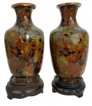Par de delicados vasos cloisonné sobre cobre, com esmaltação vítrea em tons terrosos, verdes e negros, formando composição floral estilizada. Possui perdas.Peças de fino acabamento, apresentadas sobre bases de madeira entalhada.Elegante exemplar do artesanato oriental do século XX, perfeito para compor ambientes com charme exótico e coleções de arte decorativa. Mede 21 cm.