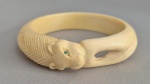 Bracelete esculpido em Marfim africano no formato de Leão mordendo a própria cauda. Olhos em pedras verdes. Medida interna: 8 cm.