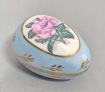 LIMOGES - Caixa oval porcelana azul claro, decorada com rosa central e detalhes dourados. Marca no fundo. Med. 10 x 7.5 x 7 cm