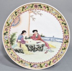Prato em porcelana chinesa, periodo Republicano, decorado com cena de cortesãs lendo co centro e borda com facha de flores e folhagens em esmaltes policromados. Marca honorífica no verso. Discreto e pequeno fio de cabelo na borda. Med. 27 cm