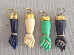 Lote com 4 pingentes de Figas baianas, sendo: 3 em baquelite marfim, verde e preto, e outra esculpida em pedra azul. Guarnições em metal dourado. Completas, com as unhas.  med. 3 cm