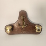 Cabideiro de parede em madeira com aplicação metálica em formato de âncora e dois suportes frontais em bronze. A peça possui estética náutica clássica, ideal para compor ambientes como escritórios, varandas, casas de praia ou decorações temáticas. Estrutura firme, com madeira de bom aspecto e ferragens que reforçam o visual tradicional.        Estado de conservação: apresenta marcas naturais do tempo e sinais de uso, sem comprometer a funcionalidade. Medindo: 25x40x10