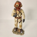 Estatueta representando mergulhador escafandrista clássico, equipado com traje de mergulho pesado e capacete metálico estilo cobre, inspirado nos modelos históricos utilizados em operações submarinas. Peça rica em detalhes, com mangueira de ar, cinto de equipamentos e base temática remetendo ao fundo do mar.