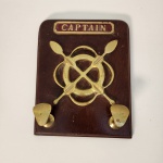 Cabideiro de parede em madeira com aplicações em Bronze representando timão e remos cruzados, encimado pela inscrição Captain. Peça de inspiração naval, com estética clássica bastante associada a ambientes marítimos e decorativos.                                                          Estado de conservação: bom estado geral, com marcas leves de uso e pátina natural nos metais. Medindo: 24x19