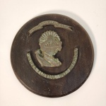 Placa militar circular composta por base de madeira escura e brasão aplicado em bronze fundido. Apresenta as inscrições em relevo Marina de Guerra del Perú e Escuela Naval del Perú, indicando vínculo direto com a marinha peruana e sua academia de formação naval.O centro exibe brasão com iconografia marítima, típico de peças institucionais utilizadas como homenagem, reconhecimento ou representação oficial. Medindo: 29x29