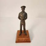 Escultura em bronze representando um marinheiro em uniforme naval clássico, com acabamento envelhecido que destaca os detalhes da peça. Está fixada sobre base de madeira em estilo deck, garantindo estabilidade e um visual elegante. Peça decorativa com temática marítima, em bom estado de conservação, apresentando apenas leves marcas naturais do tempo. Medindo: 25x10x10