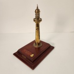 Elegante miniatura de farol marítimo produzida em metal com acabamento dourado envelhecido, montada sobre base de madeira maciça. A peça apresenta detalhes arquitetônicos bem trabalhados, como o topo em forma de lanterna e a varanda circular, remetendo aos clássicos faróis costeiros. Medindo: 30x24x19