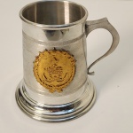Caneca comemorativa em metal prateado com aplicação frontal em relevo dourado representando um brasão militar com âncora e estrela, remetendo ao universo naval. A peça possui gravação lateral com a inscrição: Recuerdo de la Armada Boliviana en ocasión de la XVIII C.O.N.S. Brasil, R.J. Oct. 96. Montada sobre base integrada e com alça robusta, apresenta acabamento elegante e caráter institucional, típica de eventos oficiais ou encontros militares internacionais. Medindo: 14x15