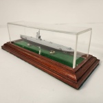 Elegante miniatura de submarino militar apresentada em vitrine de material sintético  transparente, com base em madeira e interior revestido em tecido verde. A peça possui ótimo nível de detalhamento, representando fielmente a estrutura do submarino.