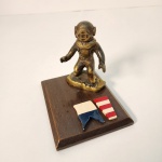 Miniatura representando um escafandro clássico de mergulho, confeccionada em bronze fundido com acabamento envelhecido que destaca os detalhes da peça. A figura está fixada sobre uma base de madeira maciça, conferindo estabilidade e elegância à composição. Medindo: 12x14x11