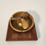 Cinzeiro com forte estética náutica e industrial, feito em bronze maciço. A hélice central dá personalidade ao objeto, funcionando tanto como cinzeiro quanto como item de decoração. Base em madeira adiciona estabilidade e charme clássico. Medindo: 7x14x13