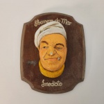 Placa em madeira com escultura em relevo representando um marinheiro com expressão irreverente, usando boina e segurando um cachimbo. A peça traz a inscrição Homem do Mar  Imediato e possui estilo artesanal, com pintura manual e traços caricatos que remetem à decoração naval clássica. Ideal para ambientes temáticos, bares ou colecionadores de itens marítimos. Medindo: 23x19