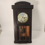 Este relógio de parede apresenta caixa robusta em madeira escura, com pátina natural que denuncia décadas de histórias silenciosas. O mostrador possui numeração clássica e elegante, protegido por vidro, enquanto o compartimento inferior revela o pêndulo, trazendo aquele charme hipnótico típico dos relógios mecânicos tradicionais. Medindo: 80x35x18