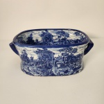 Jardineira em porcelana com clássica decoração azul e branca em cena campestre, formato oval e alças laterais. Peça elegante e versátil, com base marcada Victoria Ware Ironstone, linha reconhecida pela durabilidade e qualidade da porcelana. Medindo: 14x35x22
