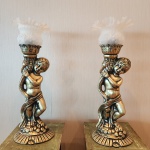 Conjunto formado por duas luminárias ornamentais executadas em bronze patinado, cada peça modelada com a figura de um putto em pose graciosa, abraçado a uma coluna de inspiração clássica, com rica textura e detalhes minuciosamente esculpidos.As luminárias são coroadas por globos em vidro leitoso opalino, com delicado relevo de uvas e folhas, finalizados por bordas onduladas que suavizam a luminosidade quando acesas. A composição remete à estética neoclássica / romântica, com forte apelo decorativo e presença cênica. ornamentais executadas em bronze patinado, cada peça modelada com a figura de um putto em pose graciosa, abraçado a uma coluna de inspiração clássica, com rica textura e detalhes minuciosamente esculpidos.. Dimensões: 64x22x15 centímetros.