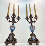 Par de candelabros em porcelana Sèvres e bronze dourado, França, séc. XIX Magnífico par de candelabros franceses em porcelana Sèvres, no clássico tom bleu céleste, com montagens em bronze dourado ricamente cinzelado. Cada peça apresenta corpo em porcelana com medalhões pintados à mão, representando delicados retratos femininos ao gosto do século XVIII, emoldurados por guirlandas e arabescos dourados. A base, igualmente adornada, ostenta cartelas ovais florais em esmalte policromado, e sustenta estrutura de quatro braços sinuosos para velas, com minucioso trabalho de fundição e acabamento. Dimensões: 45 x 17 centímetros sem velas.