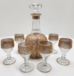 Refinado conjunto de licoreira e seis taças em cristal transparente, ricamente decorados à mão com douração em relevo, apresentando motivos florais e pássaros estilizados de inspiração otomana. A aplicação minuciosa do ouro e o brilho translúcido do cristal evidenciam o trabalho artesanal característico das oficinas turcas do século XX, unindo tradição e sofisticação. Dimensões: garrafa 27x11 centímetros, taças 11x6 centímetros.
