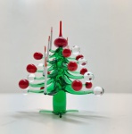 Árvore de Natal em vidro artístico Murano Encantadora escultura natalina em vidro artístico de Murano, representando uma árvore de Natal estilizada, composta por galhos em vidro verde translúcido, decorados com esferas vermelhas e transparentes, e finalizada com topo em vermelho intenso. Modelada e soprada manualmente, a peça expressa a leveza e a transparência características do vidro veneziano, combinando tradição artesanal e delicadeza decorativa. Dimensões: 6 x 5 centímetros.
