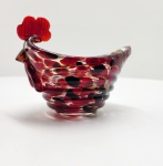 Delicada escultura em vidro artístico soprado, representando um galo estilizado, modelado manualmente em massa vítrea translúcida com nuances em vermelho, preto e dourado, obtidas pela sobreposição de camadas coloridas. O trabalho revela domínio técnico e sensibilidade cromática, típico da tradição muranesa de sopro artístico, com brilho intenso e equilíbrio formal. Dimensões: 10 x 15 x 9 centímetros.