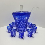 Elegante conjunto de ponche produzido em cristal overlay azul da Boêmia (Alemanha), caracterizado pelo contraste entre a camada externa azul cobalto e a lapidação profunda que revela o cristal incolor, criando desenhos geométricos e estrelas radiantes. Peça de grande presença decorativa e brilho excepcional.Acompanhado de 10 xícaras no mesmo padrão decorativo, com alças em cristal incolor, além de tampa facetada e concha também em cristal.A poncheira apresenta corpo alargado, rica lapidação em padrões losangulados, faixas cruzadas e motivos de estrela de oito pontas, típicos da produção boêmia da segunda metade do século XX. Dimensões 53x 40 centímetros