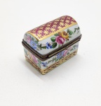 Caixinha de porcelana Limoges, marcada no fundo, modelo em formato de baú, ricamente pintada à mão com flores em tons vibrantes e frisos em ouro. A tampa em tom vinho com detalhes dourados realça o brilho da peça, que ainda conta com fecho metálico em forma de coração e interior esmaltado com motivos florais. Dimensões: 4x5x4 centímetros.