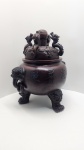 Magnífico incensário chinês de grande porte, executado em cerâmica de alta temperatura com acabamento em tonalidade castanho-escuro, imitando o aspecto do bronze tradicional. O corpo globular apresenta inscrições devocionais em chinês, associadas à proteção e purificação espiritual. As laterais são adornadas por imponentes cabeças de leões guardiões (Shi/Fu Lion) que funcionam como alças decorativas. A peça se apoia sobre três pés em forma de patas de leão, reforçando a simbologia protetiva ligada à cultura chinesa. A tampa, ricamente modelada, apresenta dragões ascendentes em alto-relevo, elementos ligados ao poder, prosperidade e energia vital. Dimensões: 60x53x40 centímetros.