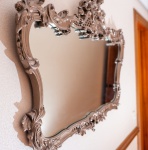 Belíssimo espelho rococó, elaborado em madeira entalhada com rica composição de elementos florais, volutas, concheados e treliças decorativas. A moldura apresenta grande destaque ornamental, especialmente no coroamento, onde flores, folhagens e curvas assimétricas se entrelaçam em um trabalho de talha volumosa e detalhada. A superfície recebeu pátina na tonalidade chumbo, aplicada para realçar os relevos e conferir aspecto envelhecido e sofisticado, compatível com o estilo elegante do período. O espelho possui oxidação natural em vários pontos. A forma sinuosa da moldura, combinada aos entalhes exuberantes, reforça a estética rococó francês.