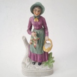 Figura de porcelana pintada à mão, representando camponesa idosa com cesto e ave. Trabalho europeu da segunda metade do século XX, com policromia fosca em tons suaves e base moldada. Peça decorativa de boa presença, típica das manufaturas populares do período. Dimensões: 30x14 x1p centímetros.